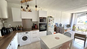 Ett kompakt kök med tvättmaskin, mikrovågsugn och en matplats med bord och stolar.