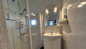Ett modernt badrum med en dusch som är avskärmad med glasväggar, ett handfat med en spegel ovanför och en papperskorg.