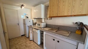 Une cuisine de taille réduite, avec des appareils électroménagers blancs, un évier et des meubles de rangement en bois.