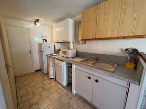 A compact kitchen with white appliances, a sink, and wooden cabinets. - Apartment with private parking - 4 guests (Fleury-Saint-Pierre-la-Mer)