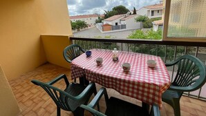 Un balcon avec une nappe à carreaux, deux chaises et une vue sur un quartier résidentiel.