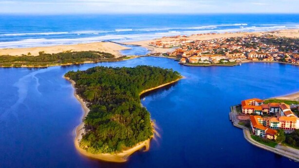 Vista aérea de un pueblo costero con una isla destacada, un puerto deportivo y edificios residenciales.