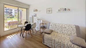 Una sala de estar con un sofá, una mesa de comedor con sillas, un ventilador y una ventana con vistas a edificios.
