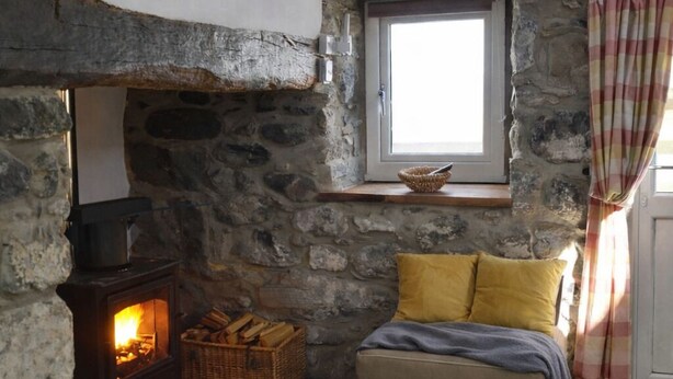 Une pièce chaleureuse avec une cheminée en pierre, un téléviseur fixé au mur, une fenêtre donnant sur un beau paysage et un lit avec des oreillers.