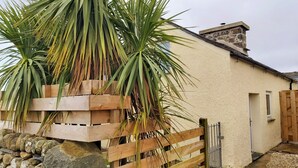 Un bâtiment avec un mur en pierre, une clôture en bois et un palmier.