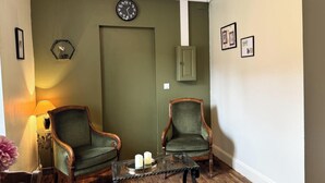 Una habitación con dos sillones tapizados en verde, una mesa de centro de madera con velas, un reloj de pared y cuadros enmarcados.