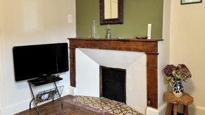 Una sala de estar con chimenea, televisor y una pequeña mesa con un florero.