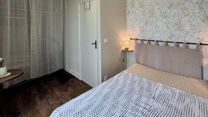 Un dormitorio con cama, mesita de noche, lámpara, puerta y un papel tapiz estampado.