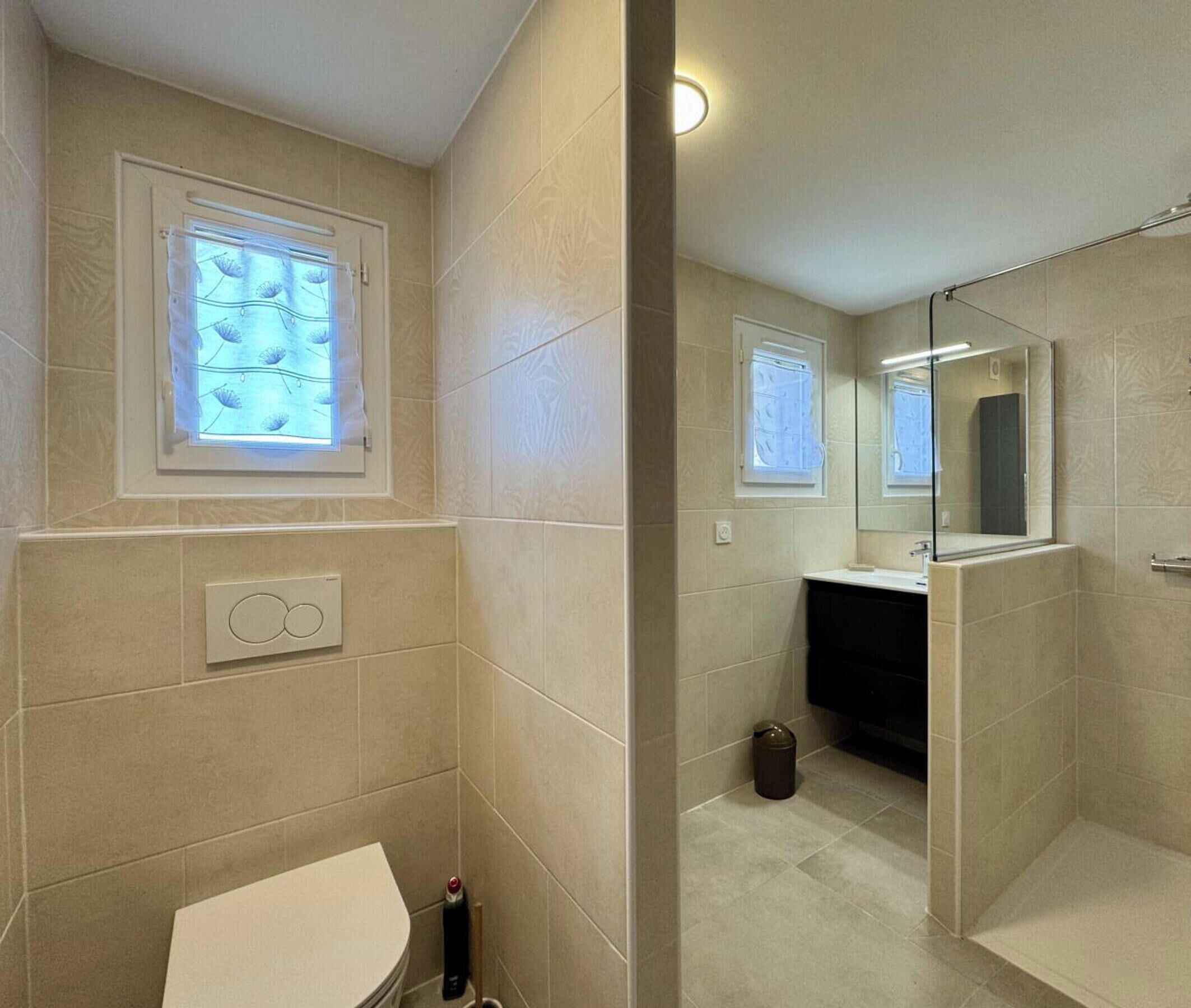 A bathroom with a toilet, a sink, a mirror, and a shower area.