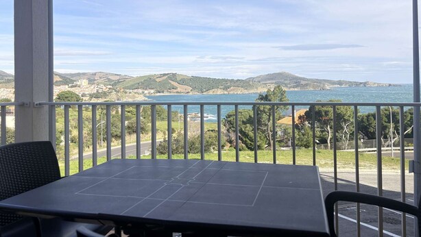 Ein Balkon mit Tisch und Stühlen, mit Blick auf eine Küstenlandschaft mit Hügeln und einem Gewässer.
