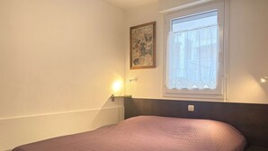Ein Schlafzimmer mit einem Bett, einem Fenster mit Vorhang, einer Wandleuchte und einem gerahmten Bild.