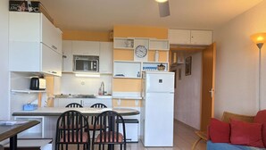Eine kompakte Küche mit weißen Schränken, einer Mikrowelle, einem Kühlschrank und einem Essbereich mit Stühlen.