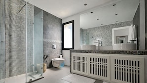 Un baño moderno con cabina de ducha de vidrio, un lavabo blanco y un espejo grande.