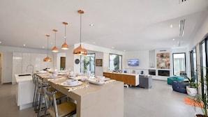 Una cocina moderna con una isla central, iluminación colgante y una zona de comedor con sillas.