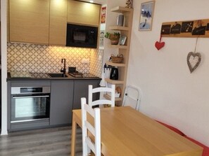 Eine kompakte Küche mit modernen Geräten, einem Esstisch mit Stühlen und einer Wand mit Bildern und herzförmigen Verzierungen.