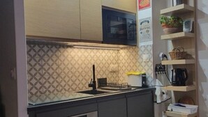 Cocina compacta con microondas, horno y pileta con grifo. Hay estantes con diversos objetos y un salpicadero con diseño.