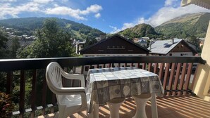 Un balcón con mesa y sillas, con vistas a un paisaje montañoso con edificios.