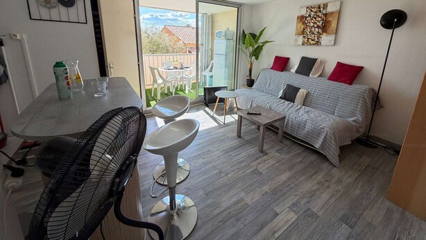 A modern living room with a dining area, a sofa set, a dining table, and a large window. - Cozy apartment with balcony - 4 guests (Narbonne)