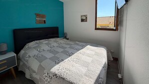 A bedroom with a bed, a nightstand, a wall-mounted TV, a window with a view, and a teal accent wall. - Cozy apartment with balcony - 4 guests (Narbonne)