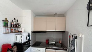 A compact kitchen with a washing machine, coffee maker, and a small shelf with various items. - Cozy apartment with balcony - 4 guests (Narbonne)