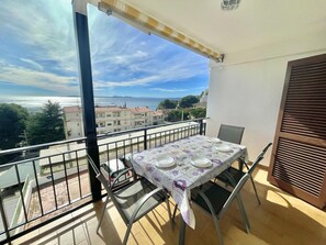 Un balcon avec une table dressée pour deux personnes, offrant une vue sur la côte et les bâtiments qui se dessinent à l’horizon.
