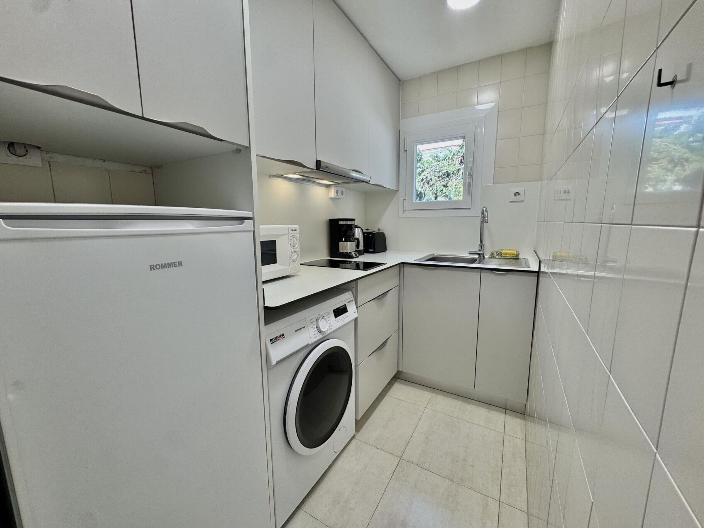 Uma cozinha compacta com máquina de lavar, micro-ondas e cafeteira.