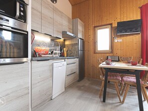 Moderni keittiö, jossa on ruostumattomasta teräksestä valmistetut kodinkoneet, puukaapit sekä ruokailutila, jossa on pöytä ja tuolit.