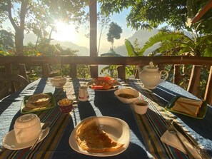 A table set with plates, bowls, and utensils, surrounded by lush greenery and a mountainous backdrop. - Bliss In Viya Ella (Ella)