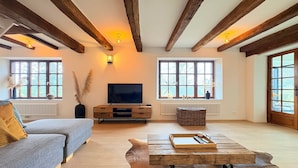 A spacious living room with a large television, wooden beams, and large windows. - Luxury Villa With Garden & Zipline (La Roche-en-Ardenne)