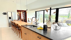 A modern kitchen with a long island, wooden cabinets, a black countertop, and a large window. - Luxury Villa With Garden & Zipline (La Roche-en-Ardenne)