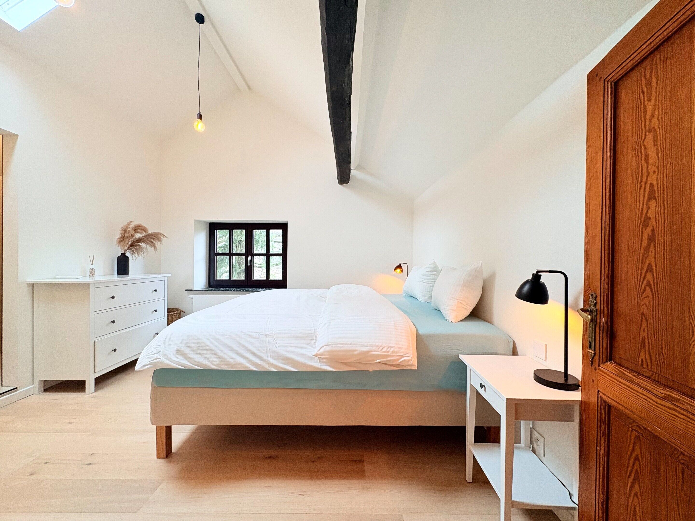 Quarto com cama, mesa de cabeceira, abajur, janela e guarda-roupa.