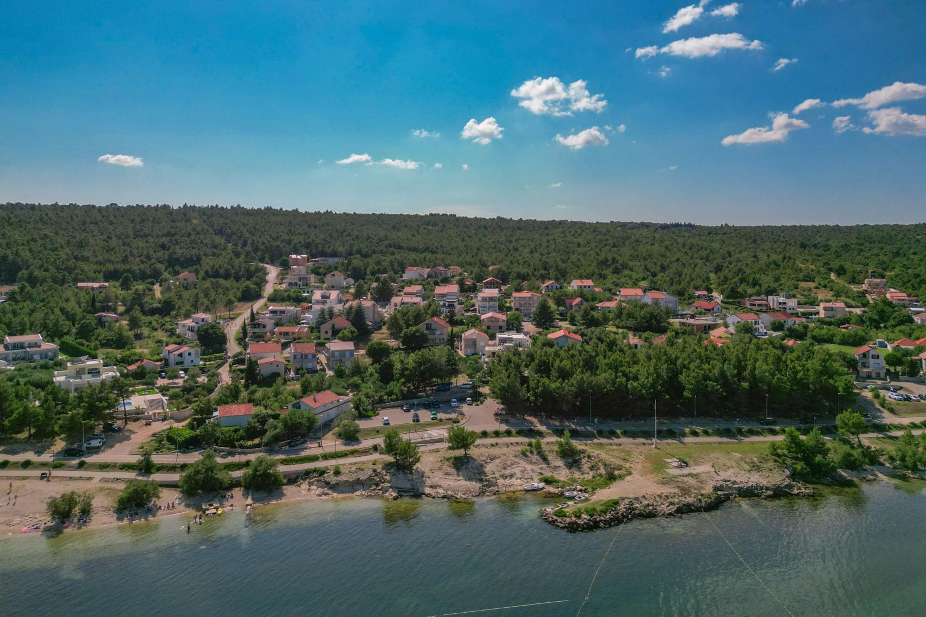 Un pueblo costero con casas, una playa y una colina boscosa.