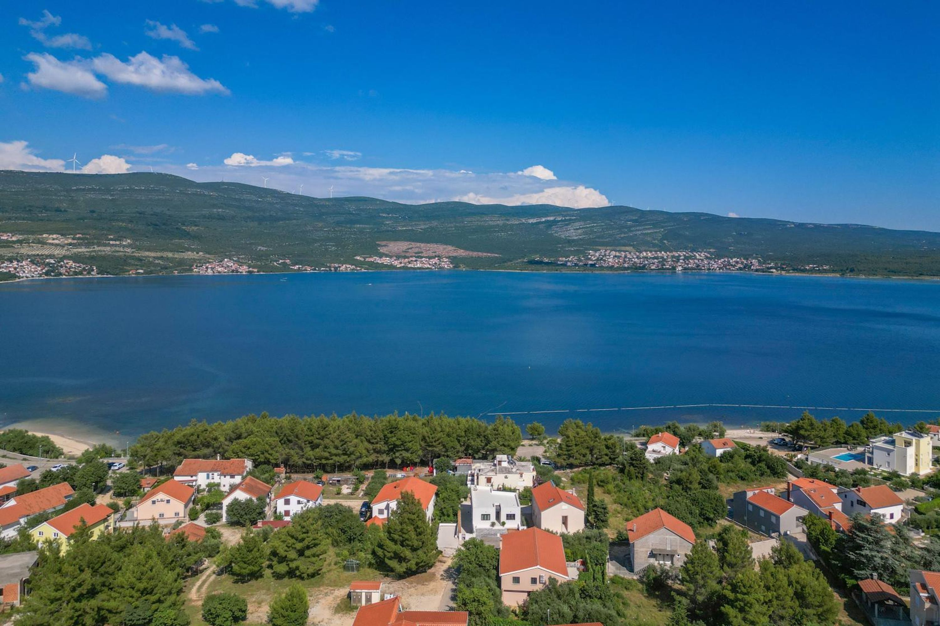 A coastal village with houses, a clear blue sea, and hills in the background.