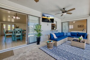 A modern living room with a sectional sofa, a dining area with a table and chairs, a ceiling fan, and a large window. - VILLA CORAL BREEZE – HEATED POOL | GULF ACCESS | BOAT RENTAL + TOURS VOUCHER INCL. (Cape Coral)