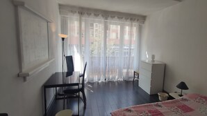Un dormitorio con cama, escritorio, silla, lámpara y ventana con cortinas.