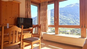 A wooden room with a TV, a chair, and large windows offering a mountain view.