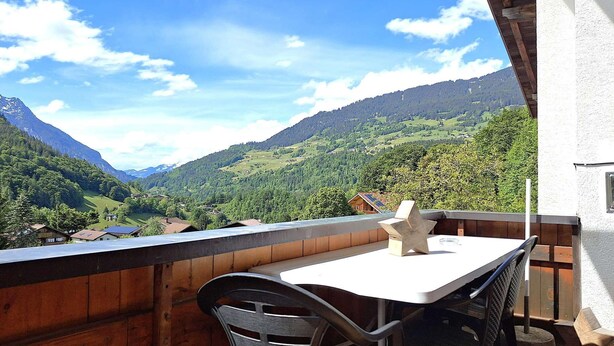 A balcony with a table and chairs overlooking a mountainous landscape.