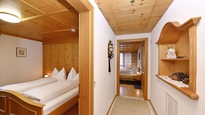 A wooden room with a bed, a shelf with decorative items, and a hallway leading to another room.