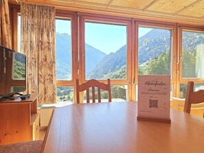 Una mesa de madera con sillas, un televisor y un cartel que dice 'Alpenfeder Gasteiger'.