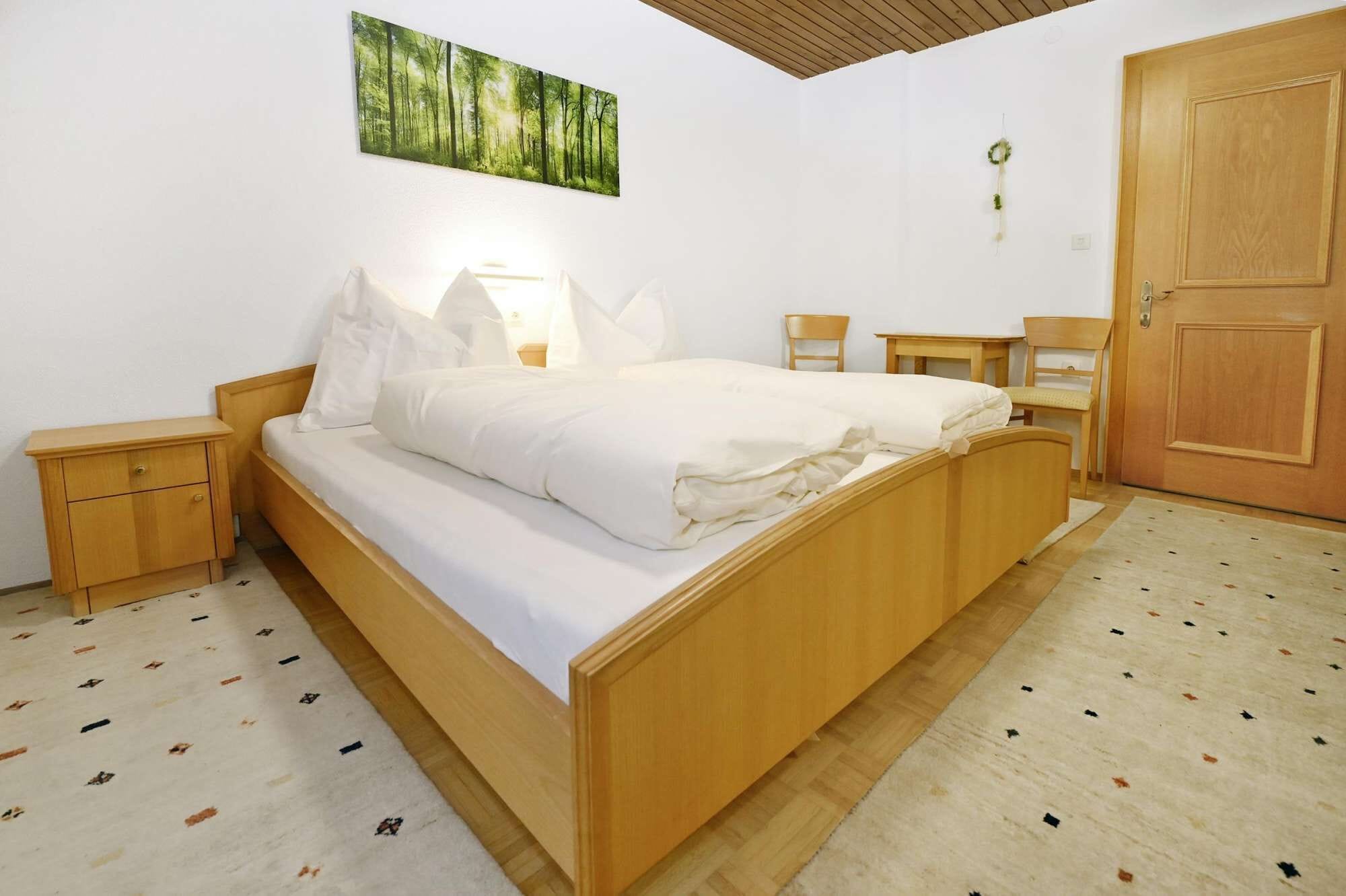 A bedroom with a wooden bed, a nightstand, a chair, a wooden door, and a wall-mounted painting.