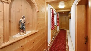 Un corridoio in legno con una statua, tende rosse a motivi decorativi e un tappeto rosso.