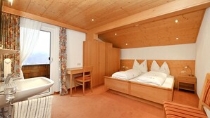 A bedroom with a wooden ceiling, a bed, a desk, a chair, a radiator, and a window with curtains. - Rundblick 5 – Spacious holiday apartment for 8 guests (Schruns-Tschagguns)