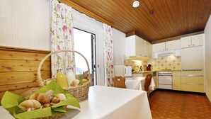 A cozy kitchen with wooden cabinets, a dining table with a basket of bread, and a view of the outdoors. - Rundblick 5 – Spacious holiday apartment for 8 guests (Schruns-Tschagguns)