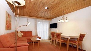 A cozy living room with a sofa, a dining table with chairs, a TV mounted on the wall, and a ceiling fan. - Rundblick 5 – Spacious holiday apartment for 8 guests (Schruns-Tschagguns)