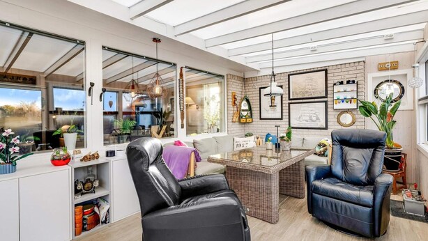 Ein modernes Wohnzimmer mit Glasdecke, einer schwarzen Ledersofa, einem Couchtisch und einem Essbereich mit Korbmöbeln.