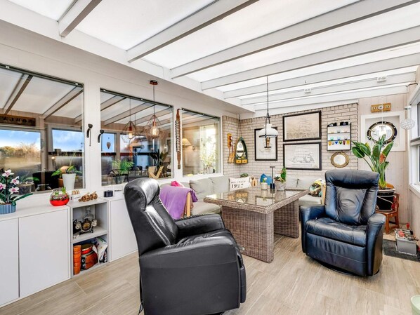 A modern living room with a glass ceiling, a black leather sofa, a coffee table, and a dining area with wicker furniture. - 4 Star Holiday Home in Lokken (Lokken)