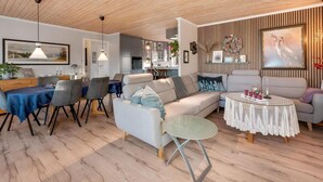 Ein modernes Wohnzimmer mit Holzboden, einem Essbereich mit blauer Tischdecke und einer Küche im Hintergrund.