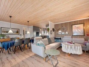 A modern living room with a wooden ceiling, a dining area with a blue tablecloth, and a kitchen in the background. - 4 Star Holiday Home in Lokken (Lokken)
