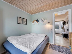A bedroom with a bed, a wall-mounted shelf with books, a wall-mounted light, and a door leading to a bathroom. - 4 Star Holiday Home in Lokken (Lokken)
