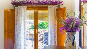 Una habitación con puerta de madera, cortinas de encaje y un jarrón con flores moradas.